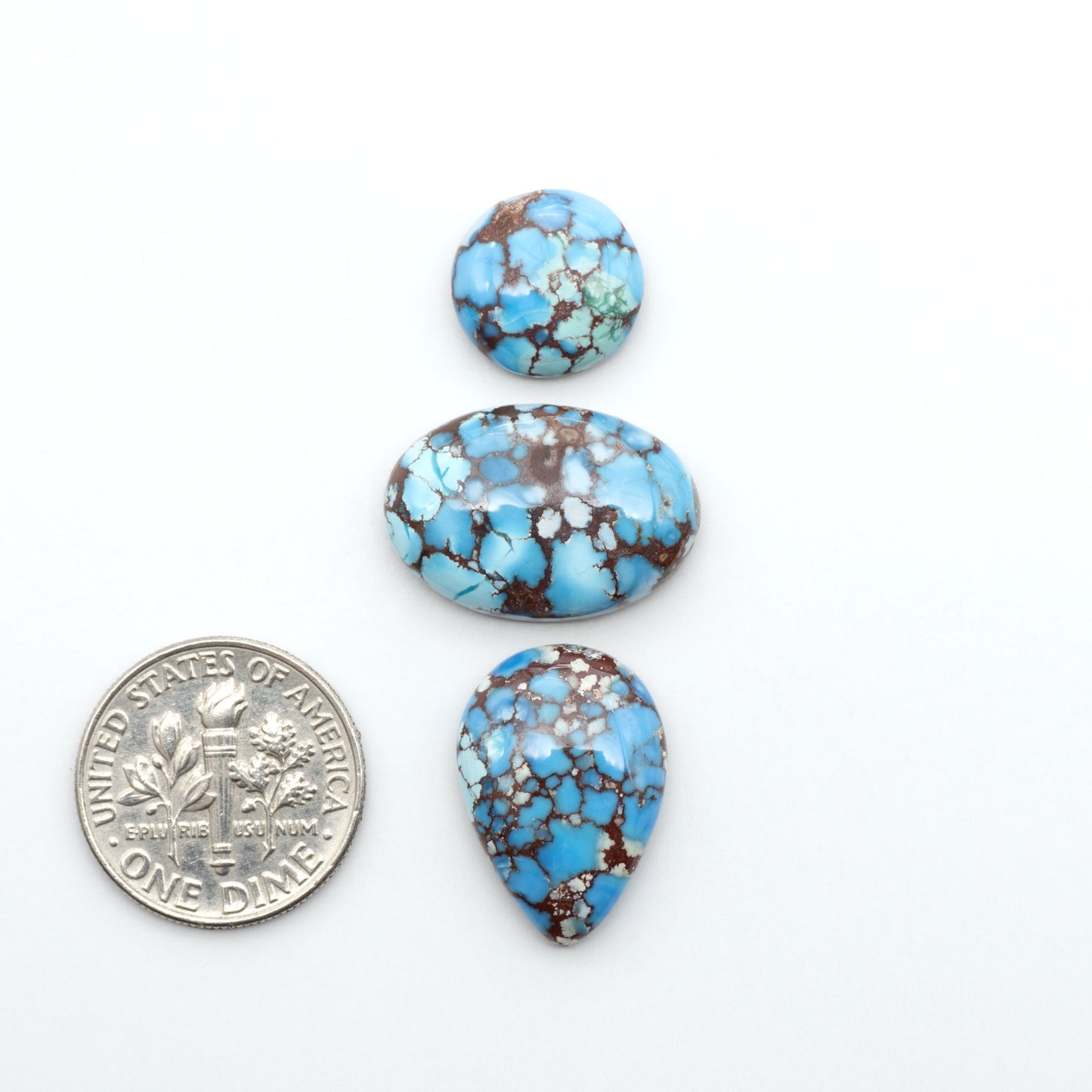 Golden Hills Turquoise cabochons, icy blue to lavender tones with chocolate matrix, polished stones on a white background with a US dime for scale