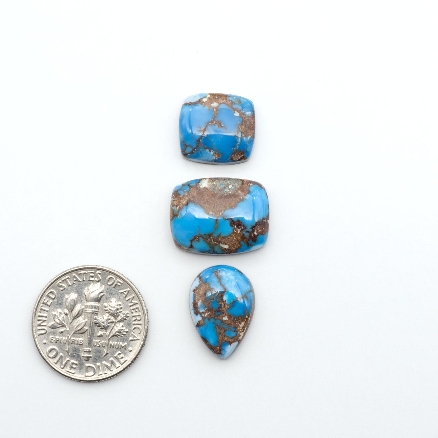 Golden Hills Turquoise cabochons, icy blue to lavender tones with chocolate matrix, polished stones on a white background with a US dime for scale