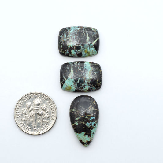 Black Jack turquoise cabochons, blue-green color with black matrix, polished stones on a white background with a US dime for scale
