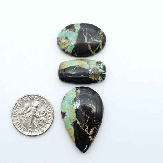Black Jack turquoise cabochons, blue-green color with black matrix, polished stones on a white background with a US dime for scale