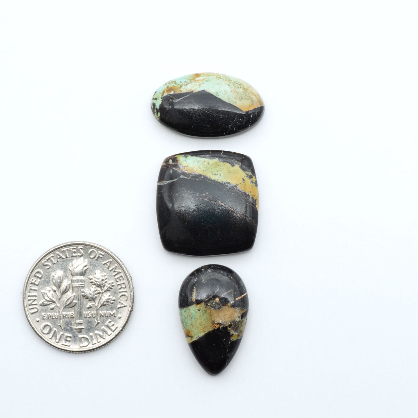Black Jack turquoise cabochons, blue-green color with black matrix, polished stones on a white background with a US dime for scale