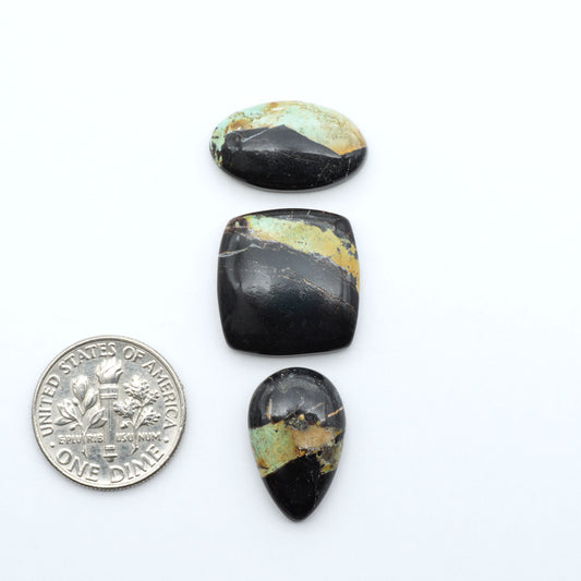 Black Jack turquoise cabochons, blue-green color with black matrix, polished stones on a white background with a US dime for scale