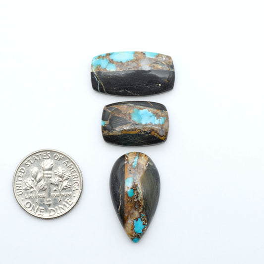 Black Jack turquoise cabochons, blue-green color with black matrix, polished stones on a white background with a US dime for scale