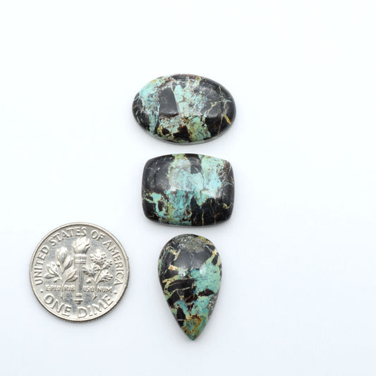 Black Jack turquoise cabochons, blue-green color with black matrix, polished stones on a white background with a US dime for scale