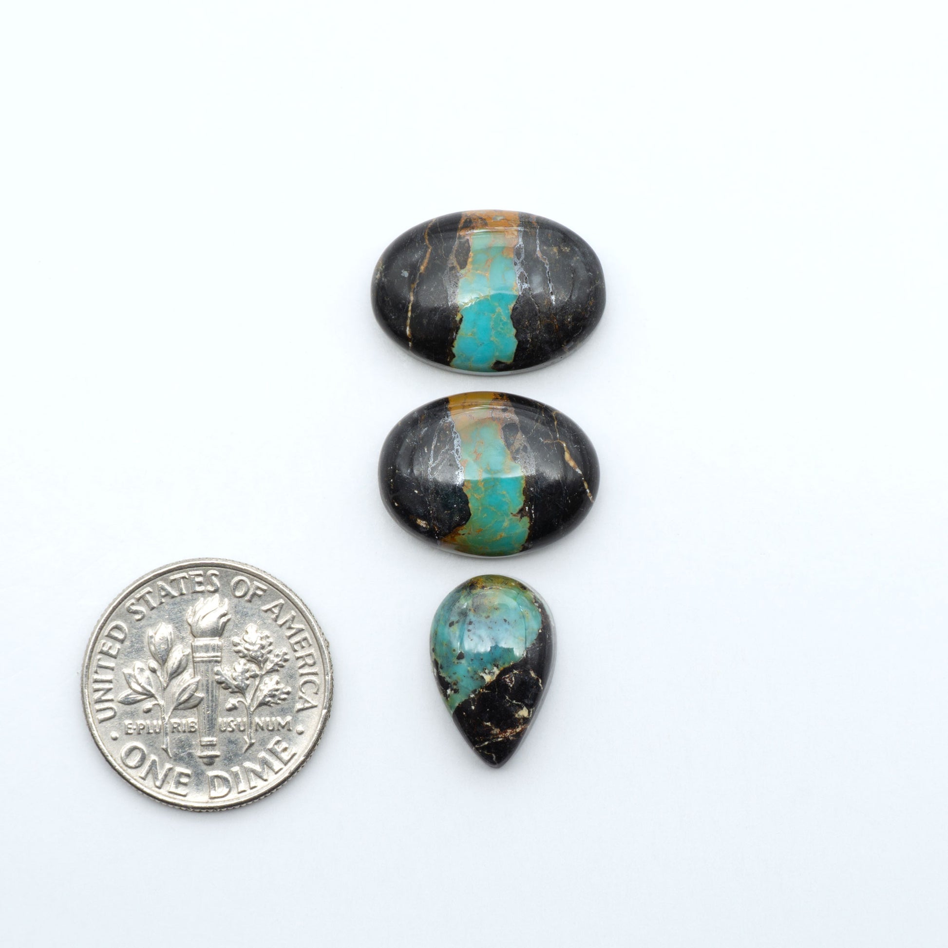 Black Jack turquoise cabochons, blue-green color with black matrix, polished stones on a white background with a US dime for scale