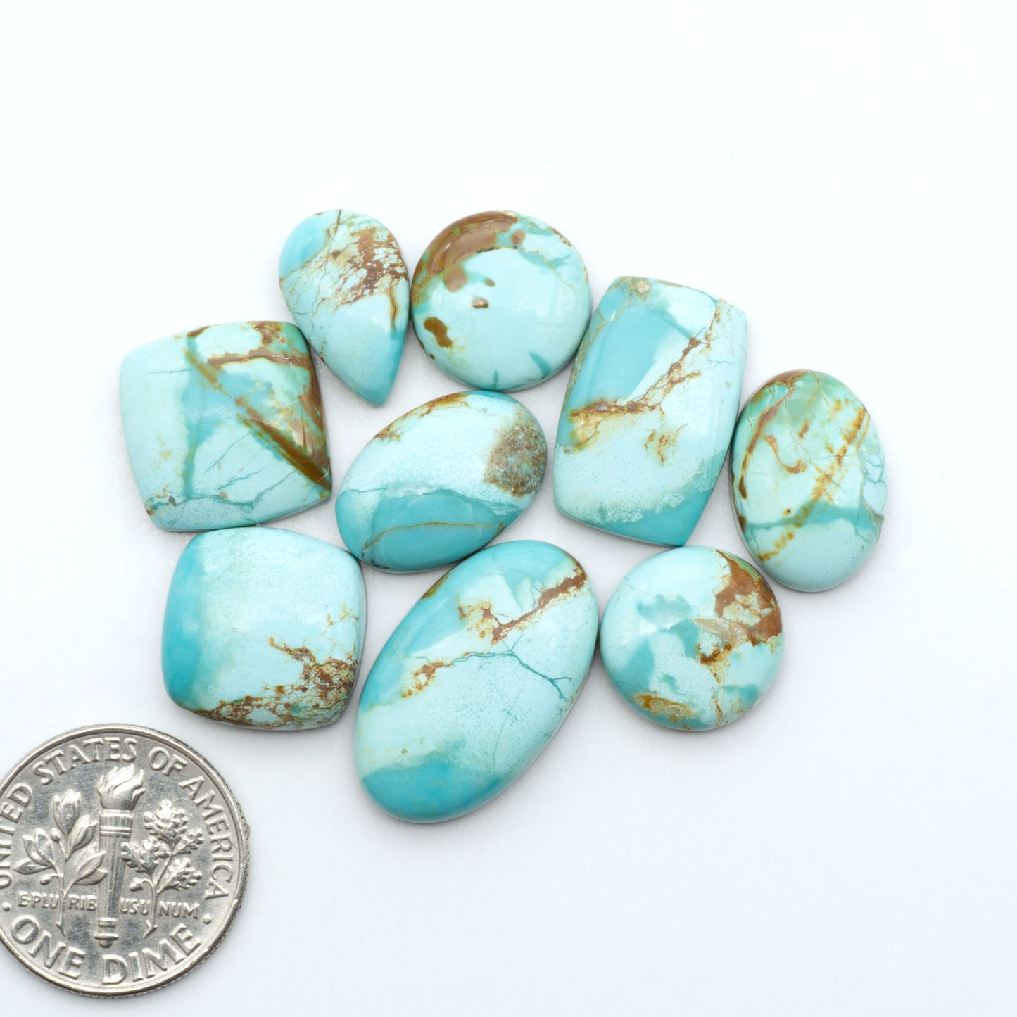 Pilot Mountain Turquoise cabochons, blue-green gemstones with natural matrix on a white background with a US dime for scale