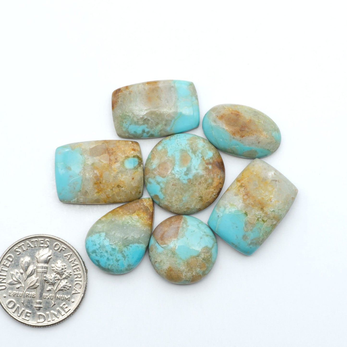 Pilot Mountain Turquoise cabochons, blue-green gemstones with natural matrix on a white background with a US dime for scale