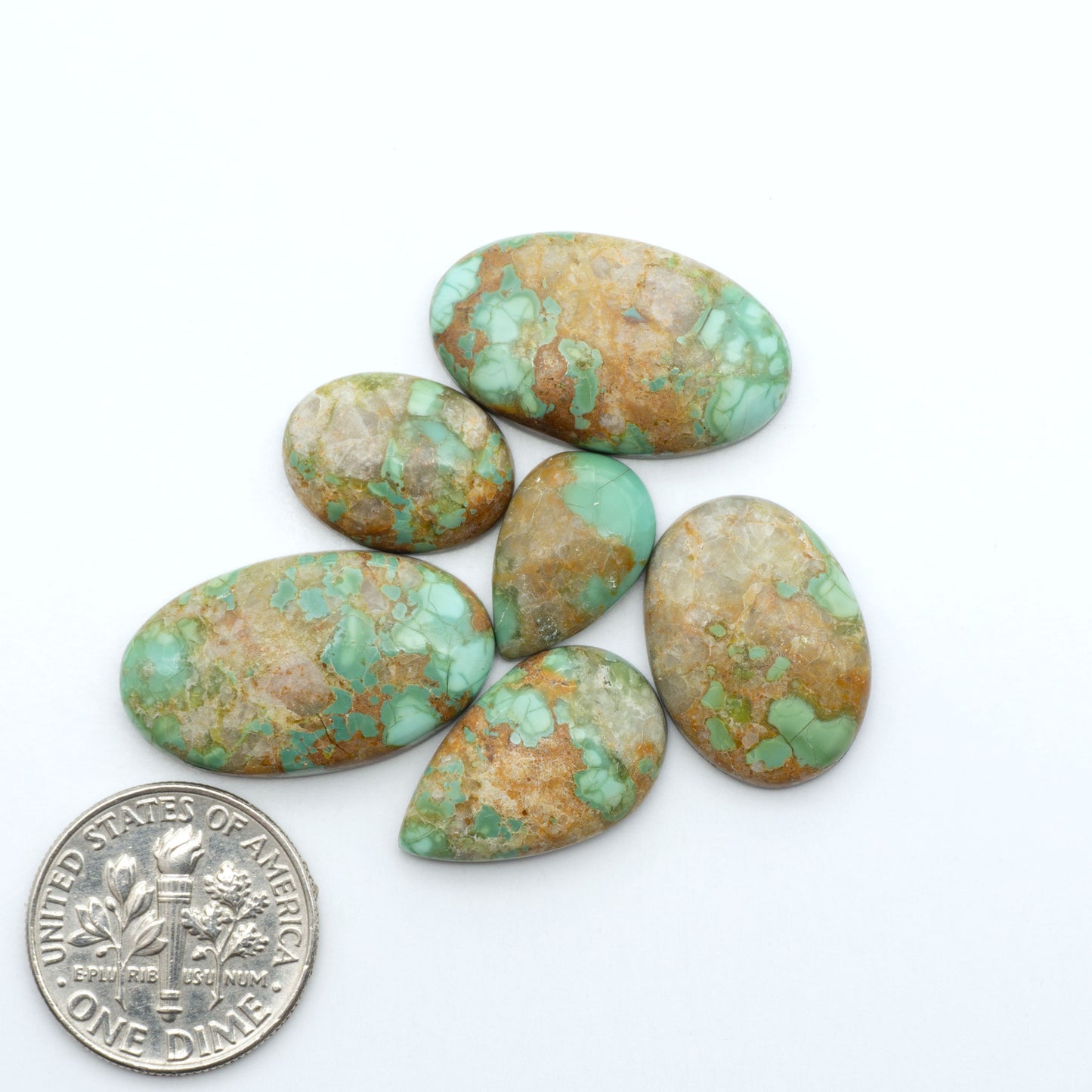 Pilot Mountain Turquoise cabochons, blue-green gemstones with natural matrix on a white background with a US dime for scale