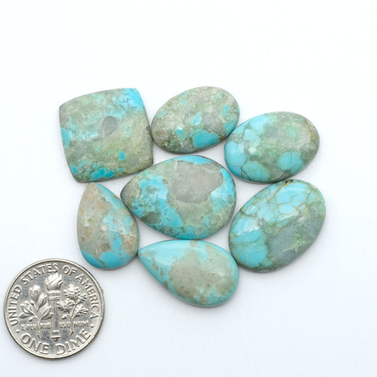 Pilot Mountain Turquoise cabochons, blue-green gemstones with natural matrix on a white background with a US dime for scale