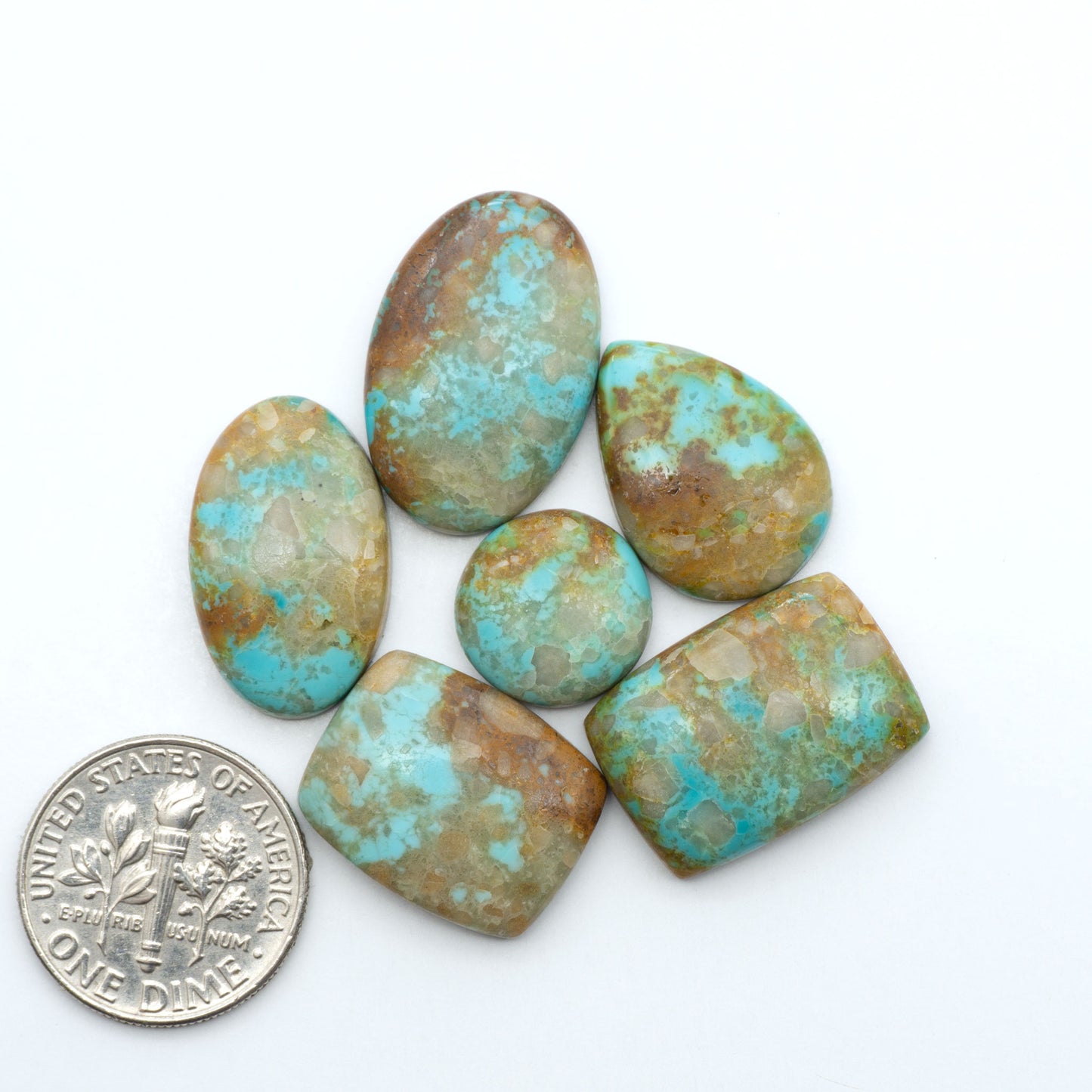 Pilot Mountain Turquoise cabochons, blue-green gemstones with natural matrix on a white background with a US dime for scale