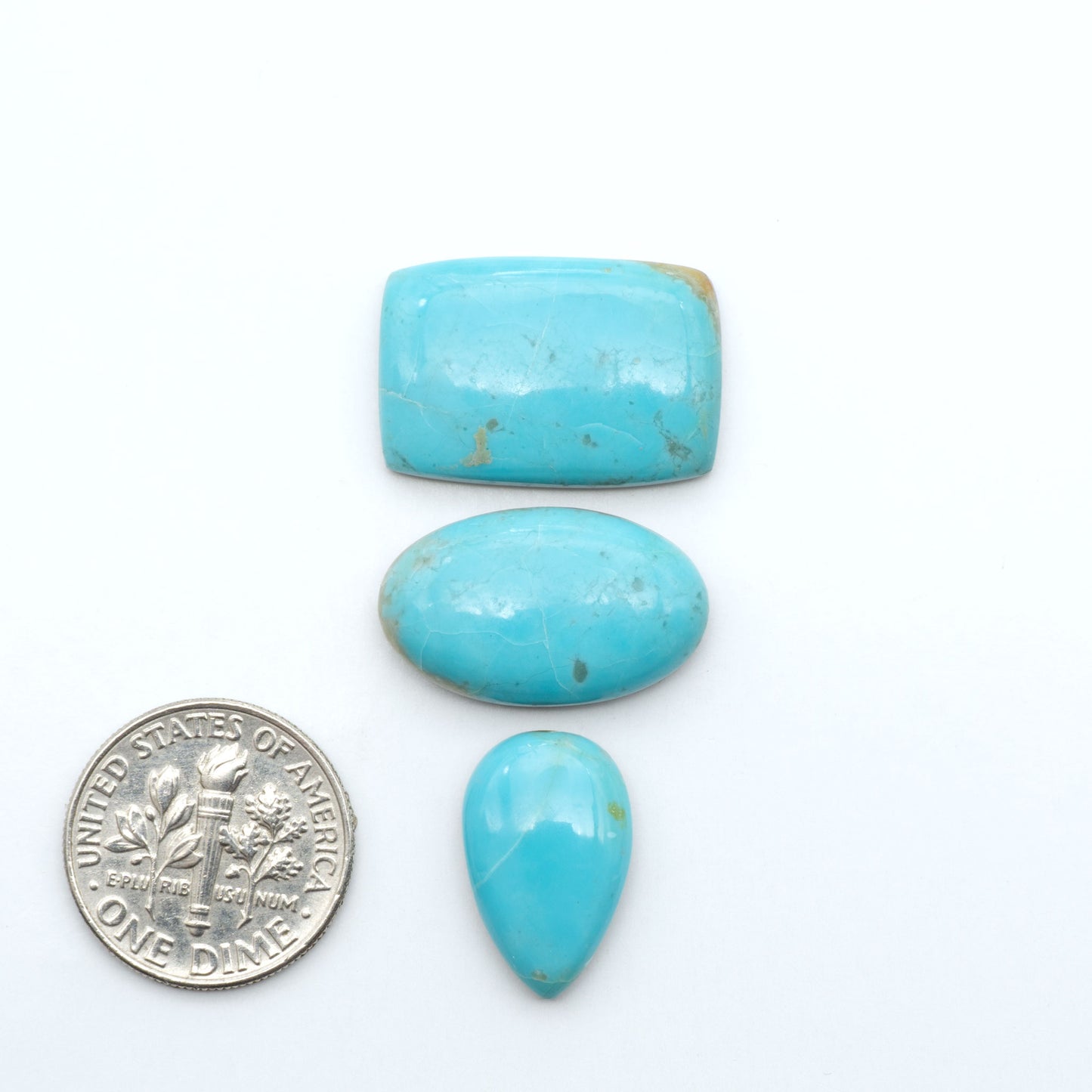 Pilot Mountain Turquoise cabochons, blue-green gemstones with natural matrix on a white background with a US dime for scale