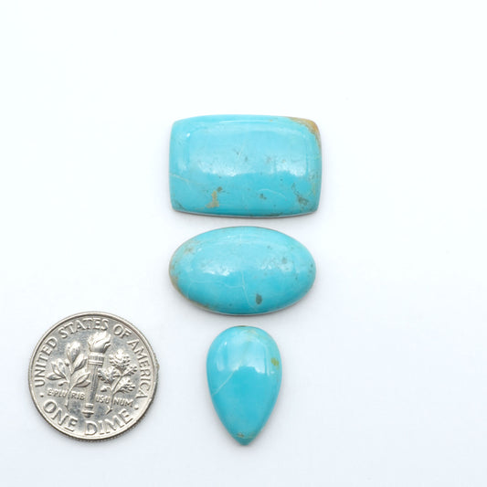 Pilot Mountain Turquoise cabochons, blue-green gemstones with natural matrix on a white background with a US dime for scale