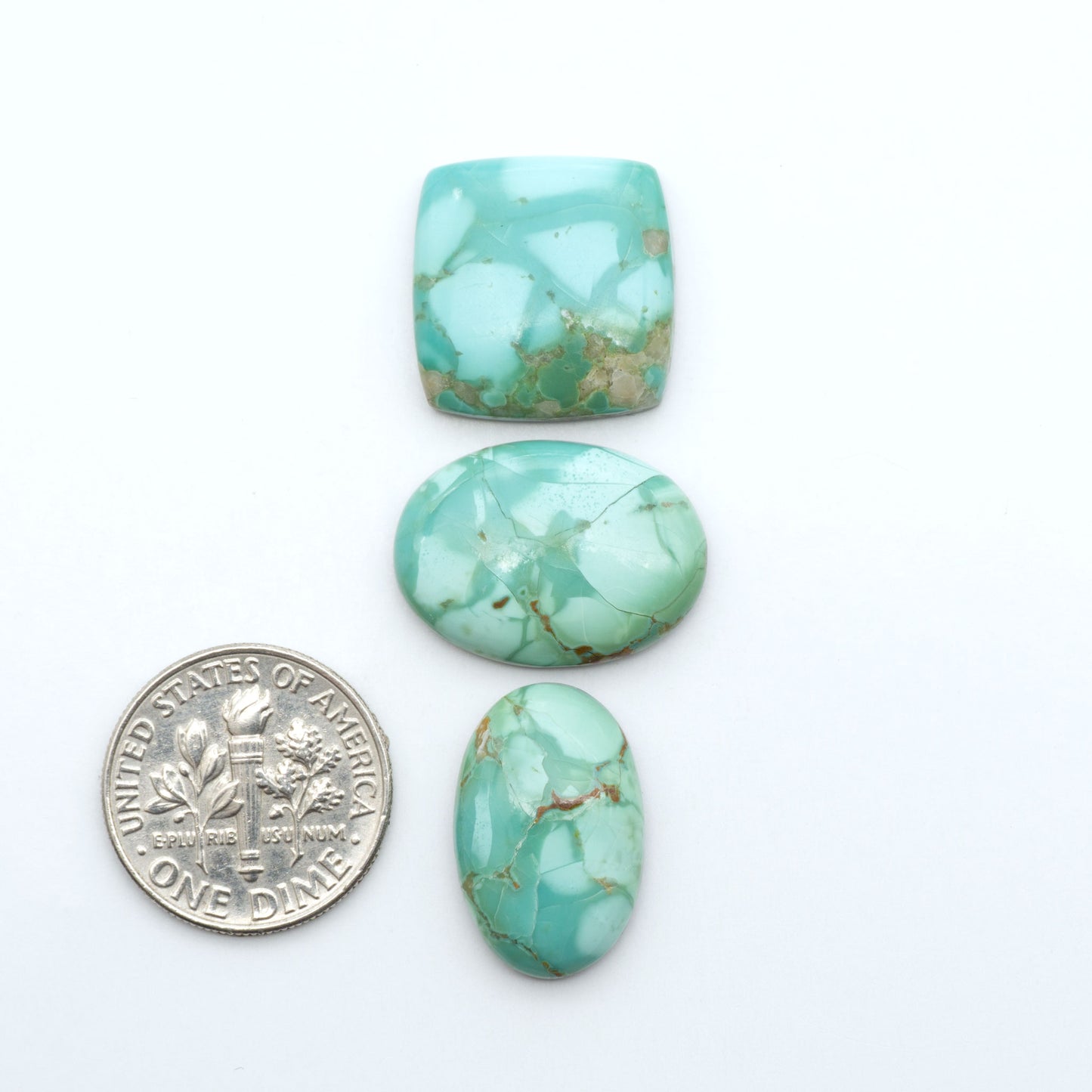 Pilot Mountain Turquoise cabochons, blue-green gemstones with natural matrix on a white background with a US dime for scale