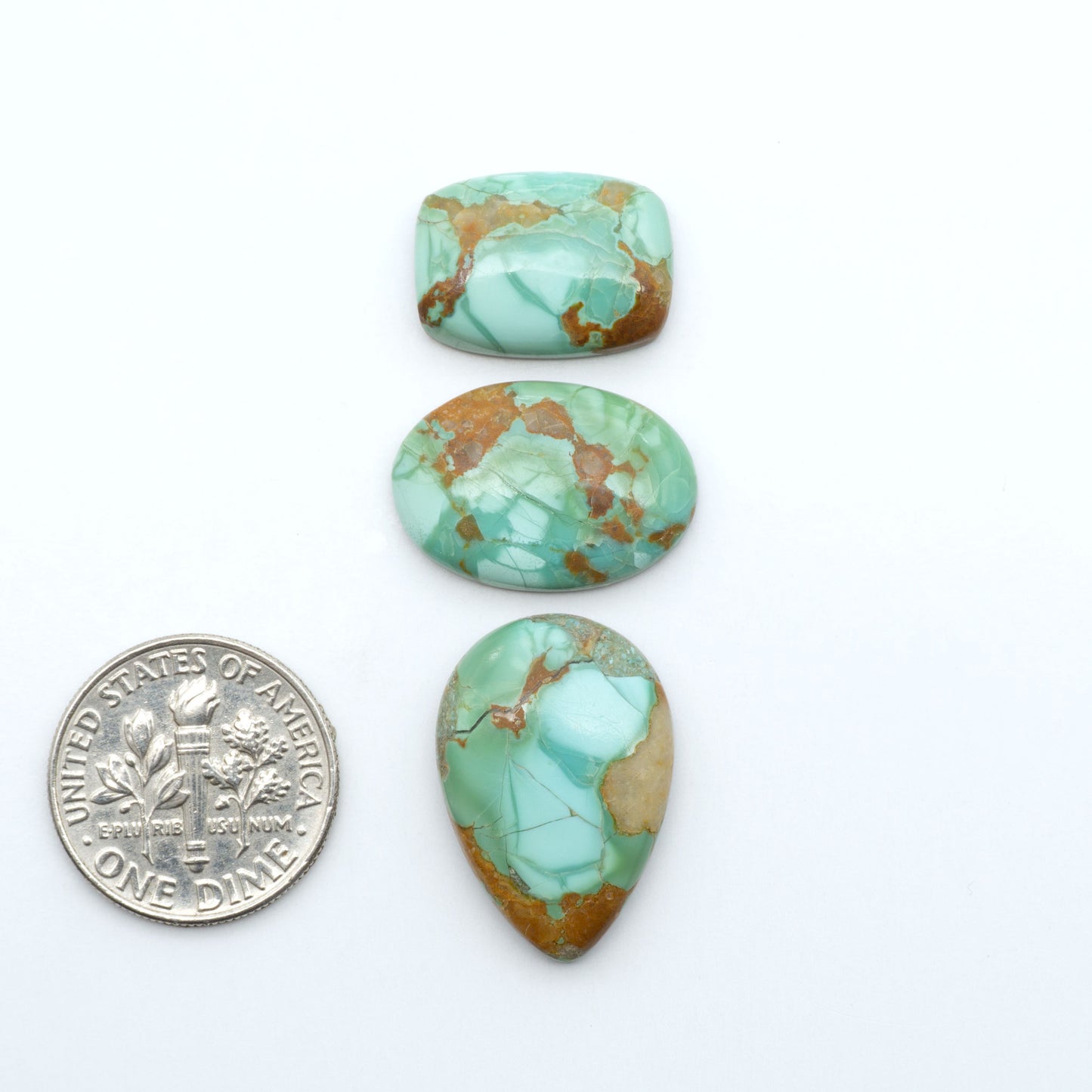 Pilot Mountain Turquoise cabochons, blue-green gemstones with natural matrix on a white background with a US dime for scale