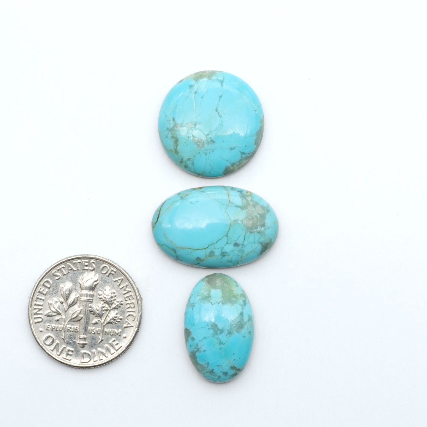 Pilot Mountain Turquoise cabochons, blue-green gemstones with natural matrix on a white background with a US dime for scale