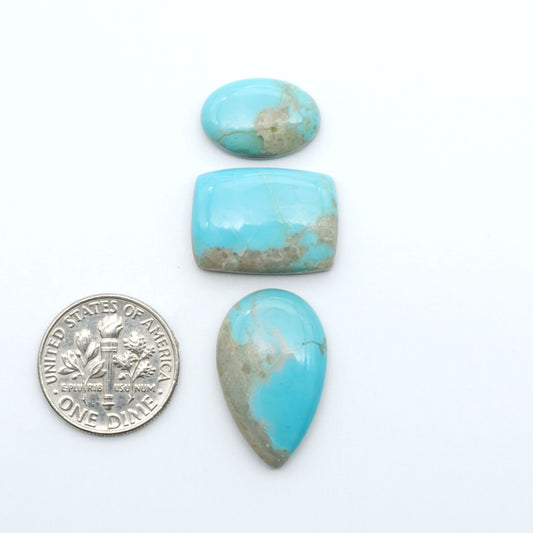 Pilot Mountain Turquoise cabochons, blue-green gemstones with natural matrix on a white background with a US dime for scale