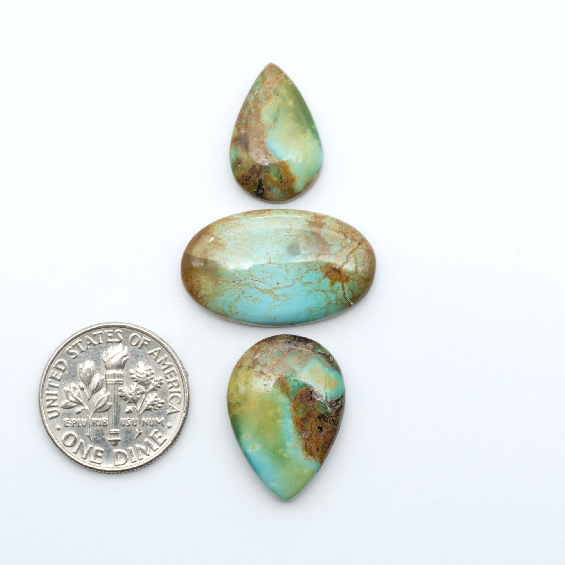 Pilot Mountain Turquoise cabochons, blue-green gemstones with natural matrix on a white background with a US dime for scale