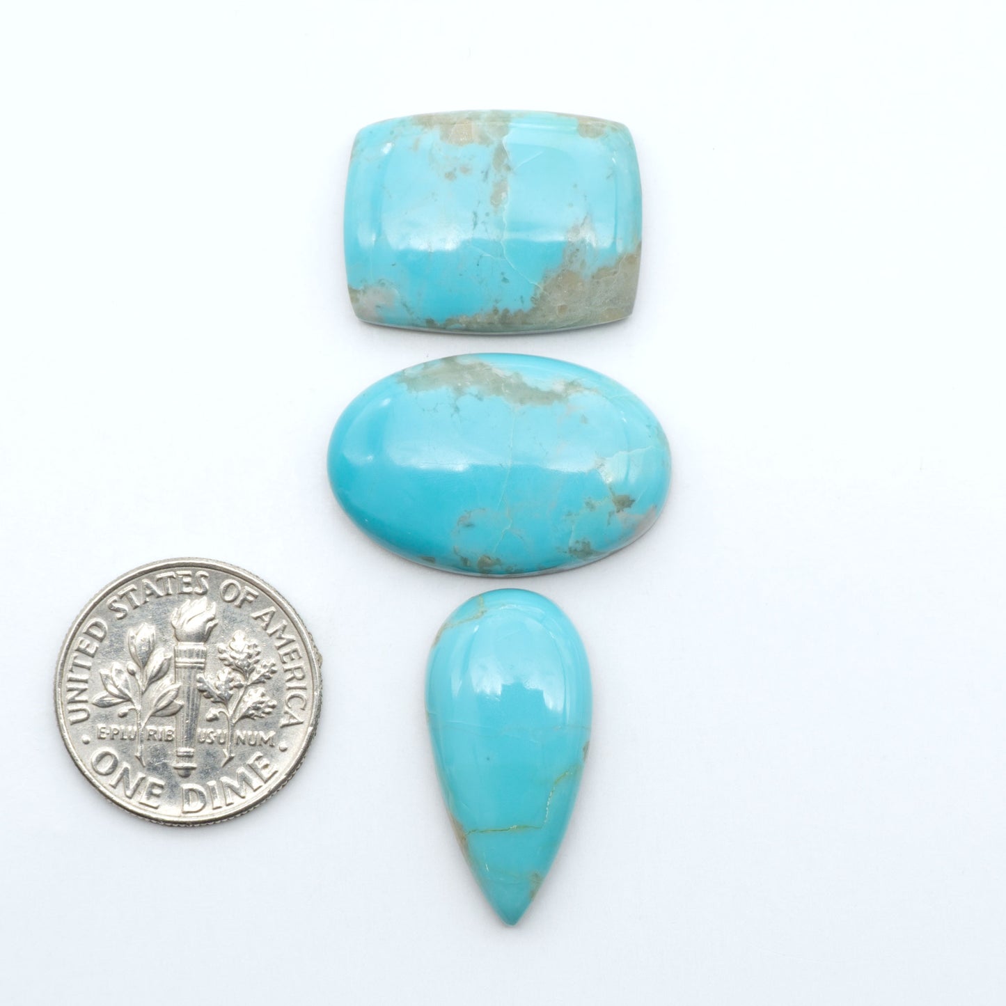 Pilot Mountain Turquoise cabochons, blue-green gemstones with natural matrix on a white background with a US dime for scale