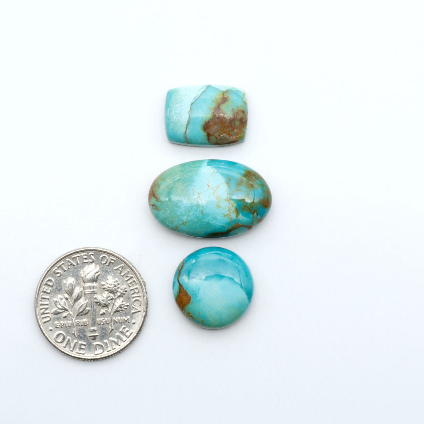 Pilot Mountain Turquoise cabochons, blue-green gemstones with natural matrix on a white background with a US dime for scale