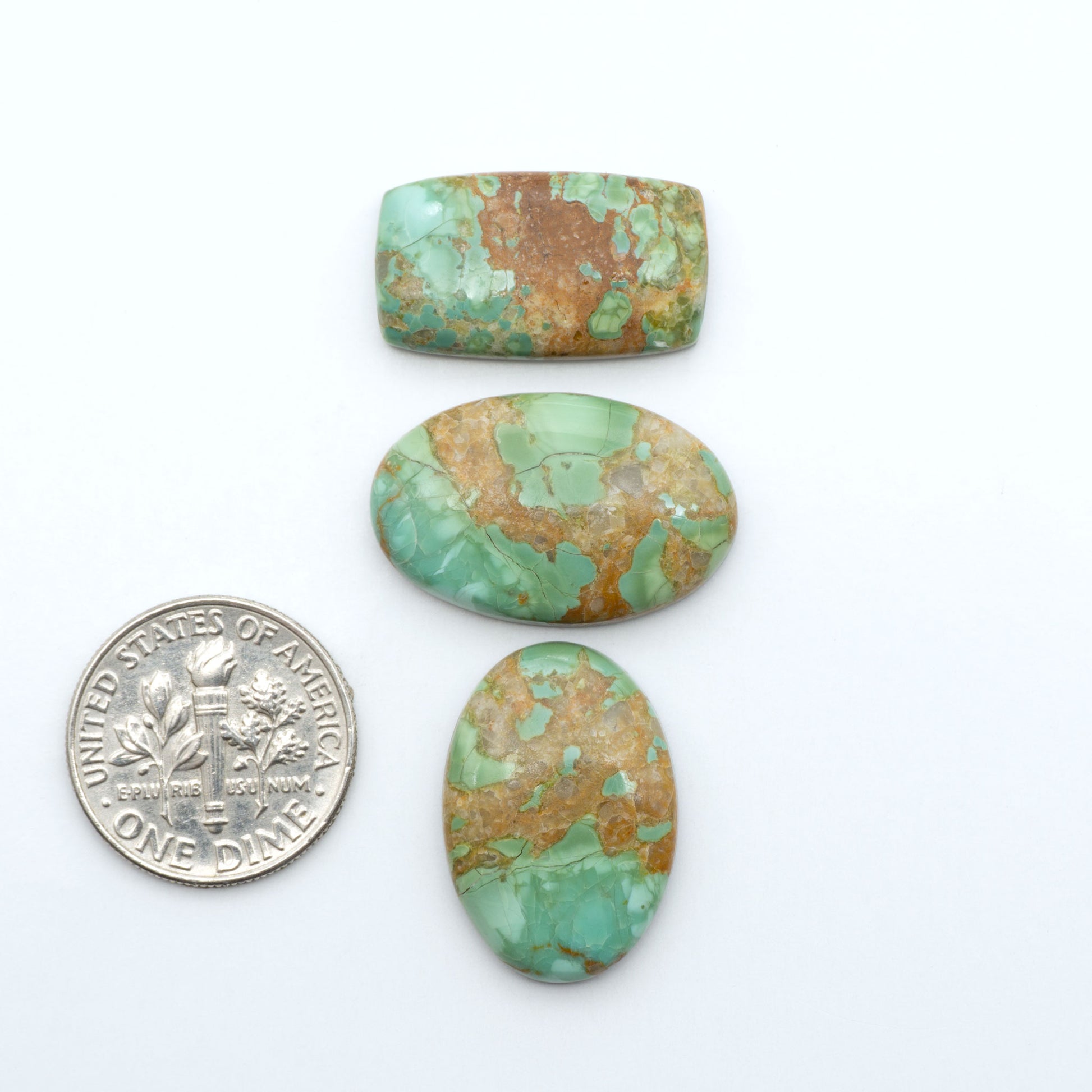 Pilot Mountain Turquoise cabochons, blue-green gemstones with natural matrix on a white background with a US dime for scale