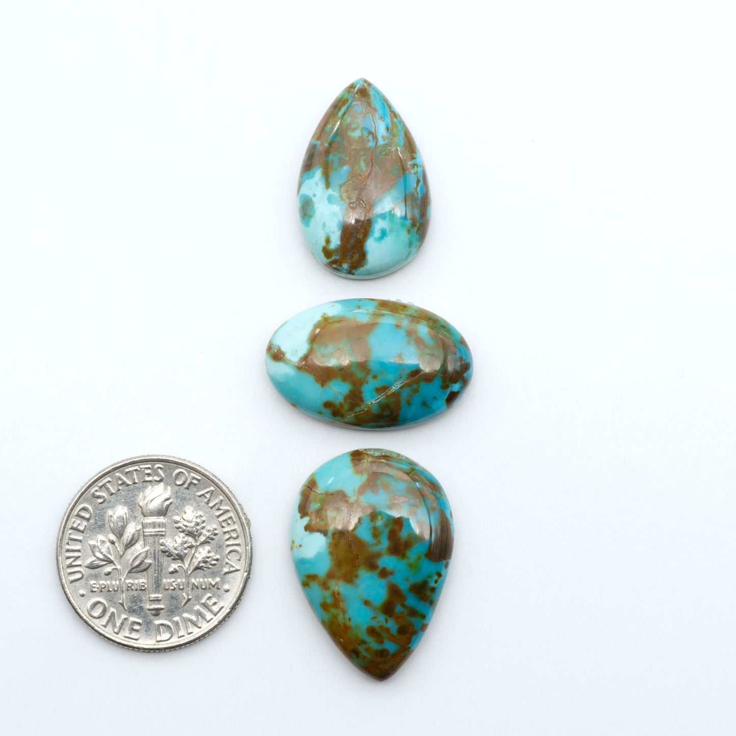 Pilot Mountain Turquoise cabochons, blue-green gemstones with natural matrix on a white background with a US dime for scale