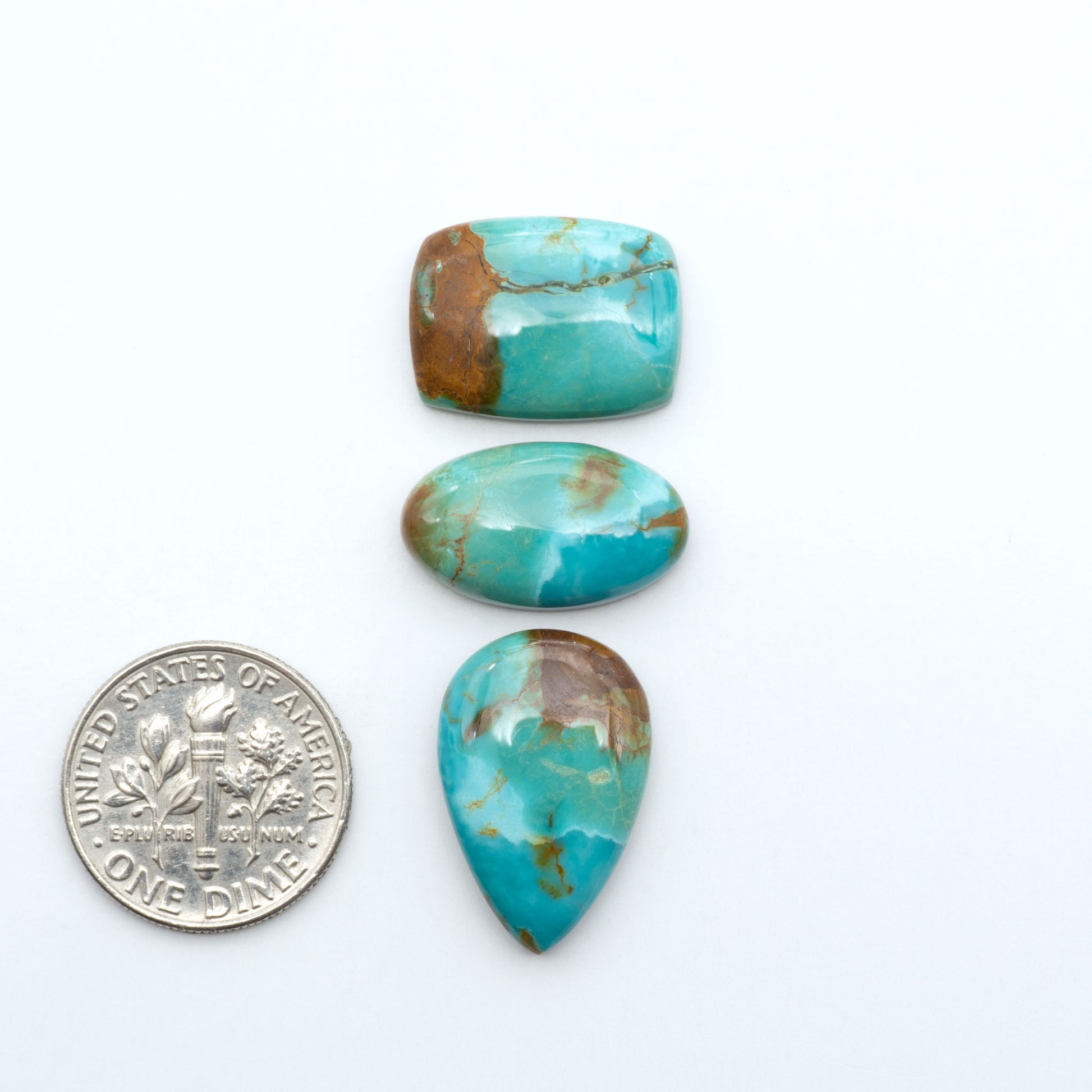 Pilot Mountain Turquoise cabochons, blue-green gemstones with natural matrix on a white background with a US dime for scale