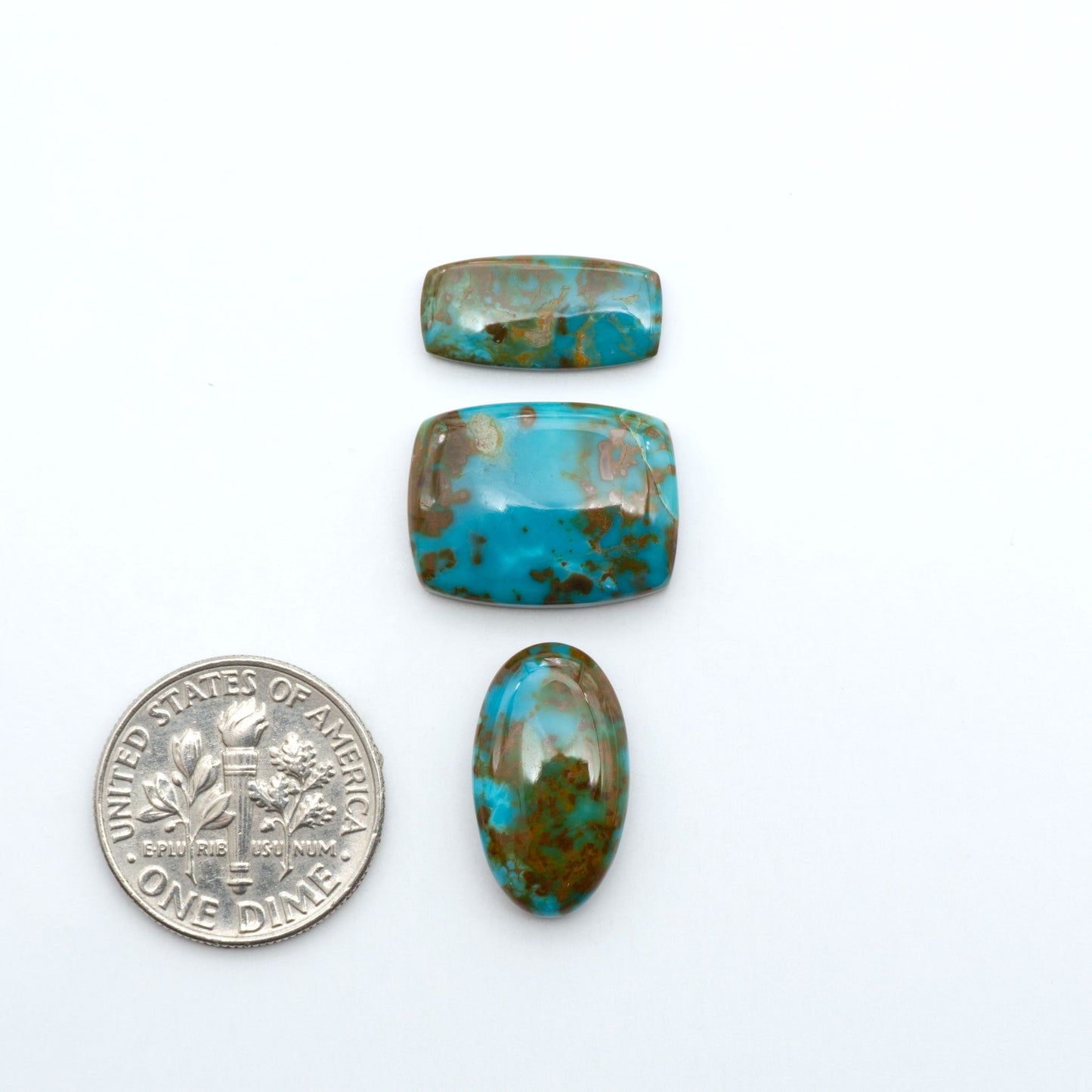 Pilot Mountain Turquoise cabochons, blue-green gemstones with natural matrix on a white background with a US dime for scale