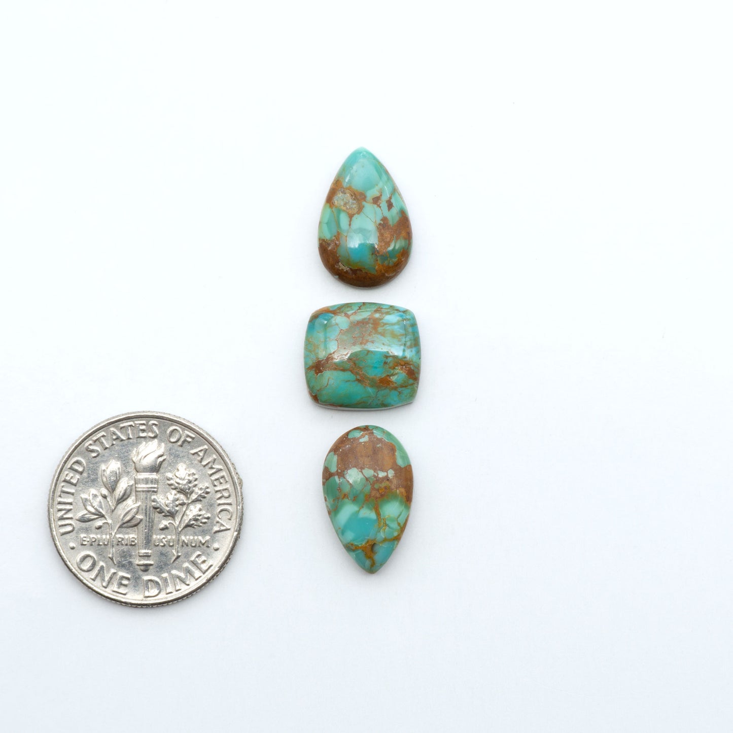 Pilot Mountain Turquoise cabochons, blue-green gemstones with natural matrix on a white background with a US dime for scale