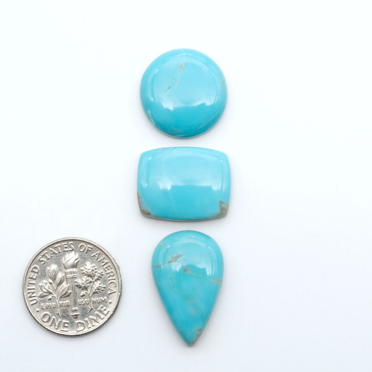 Pilot Mountain Turquoise cabochons, blue-green gemstones with natural matrix on a white background with a US dime for scale
