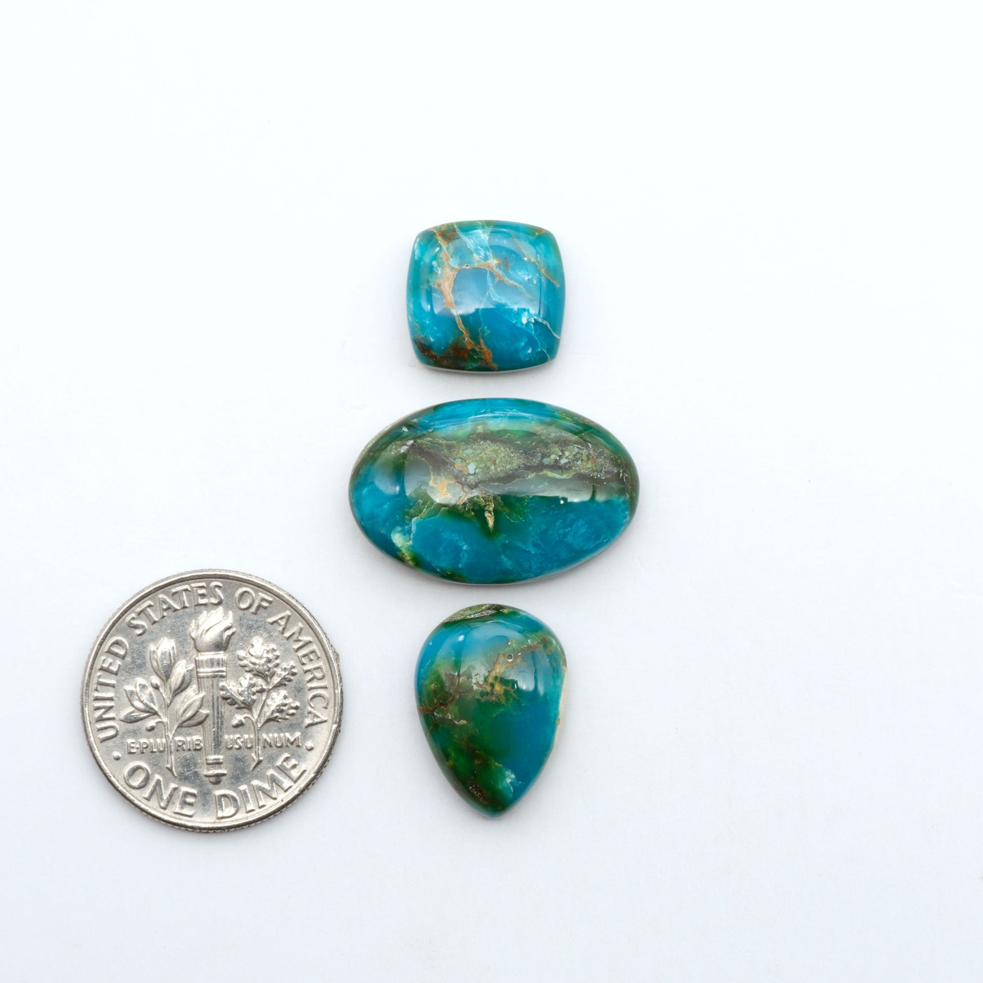 Sonoran Mountain Turquoise cabochons, blue-green color with natural matrix, polished stones on a white background, with a US dime for scale