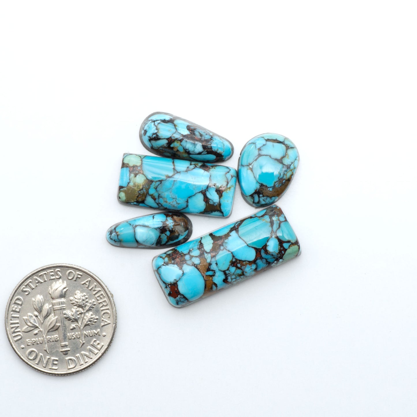 Pressed Turquoise nugget cabochons, composite material with a blue color and dark matrix on a white background, with a US dime for scale.
