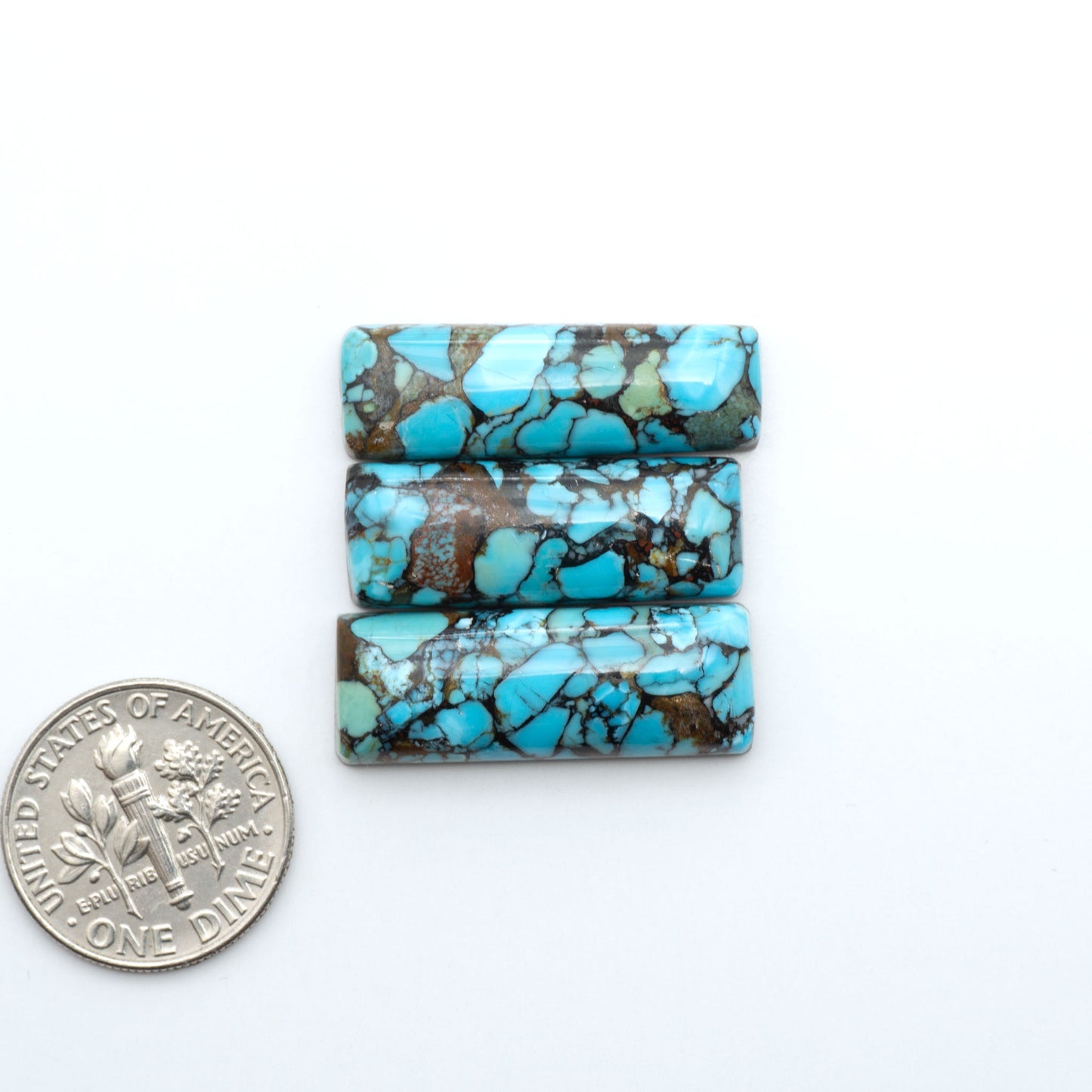 Pressed Turquoise nugget cabochons, composite material with a blue color and dark matrix on a white background, with a US dime for scale.