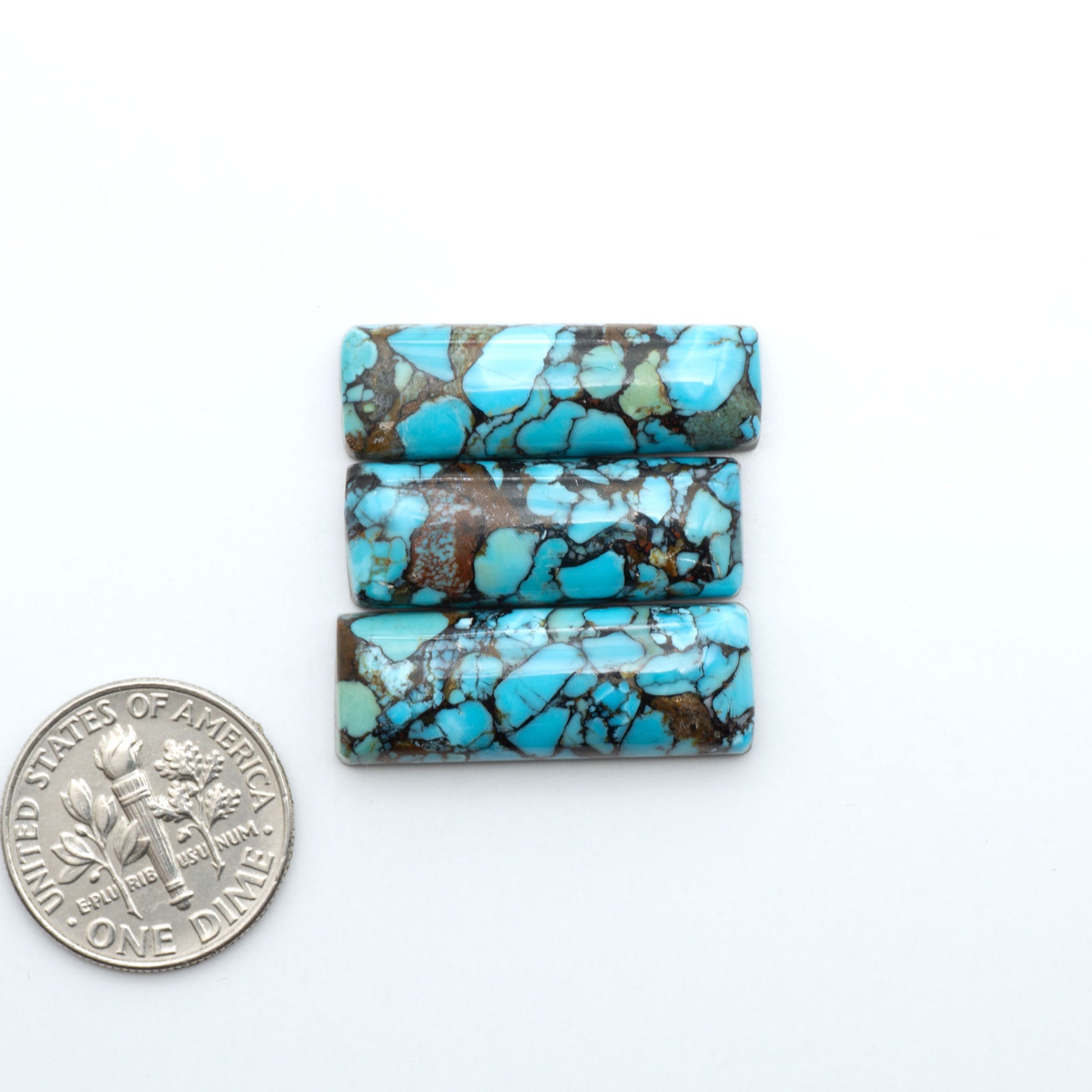 Pressed Turquoise nugget cabochons, composite material with a blue color and dark matrix on a white background, with a US dime for scale.