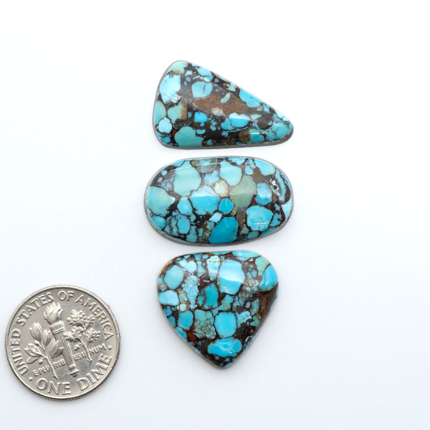 Pressed Turquoise nugget cabochons, composite material with a blue color and dark matrix on a white background, with a US dime for scale.