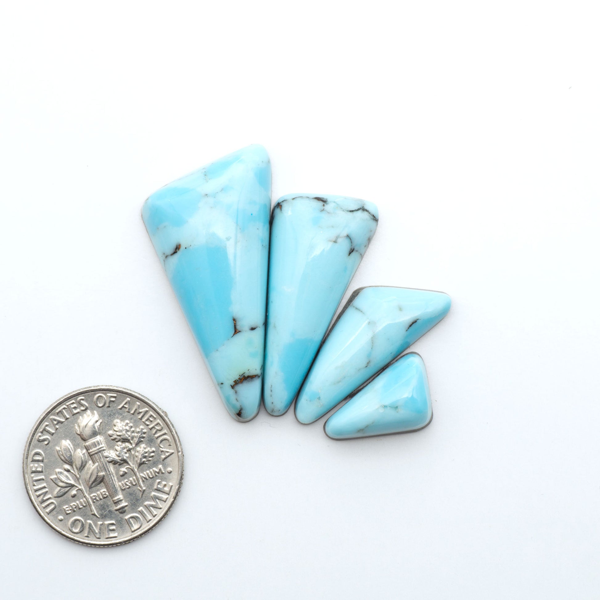 Pressed Turquoise nugget cabochons, composite material with a blue color and dark matrix on a white background, with a US dime for scale.