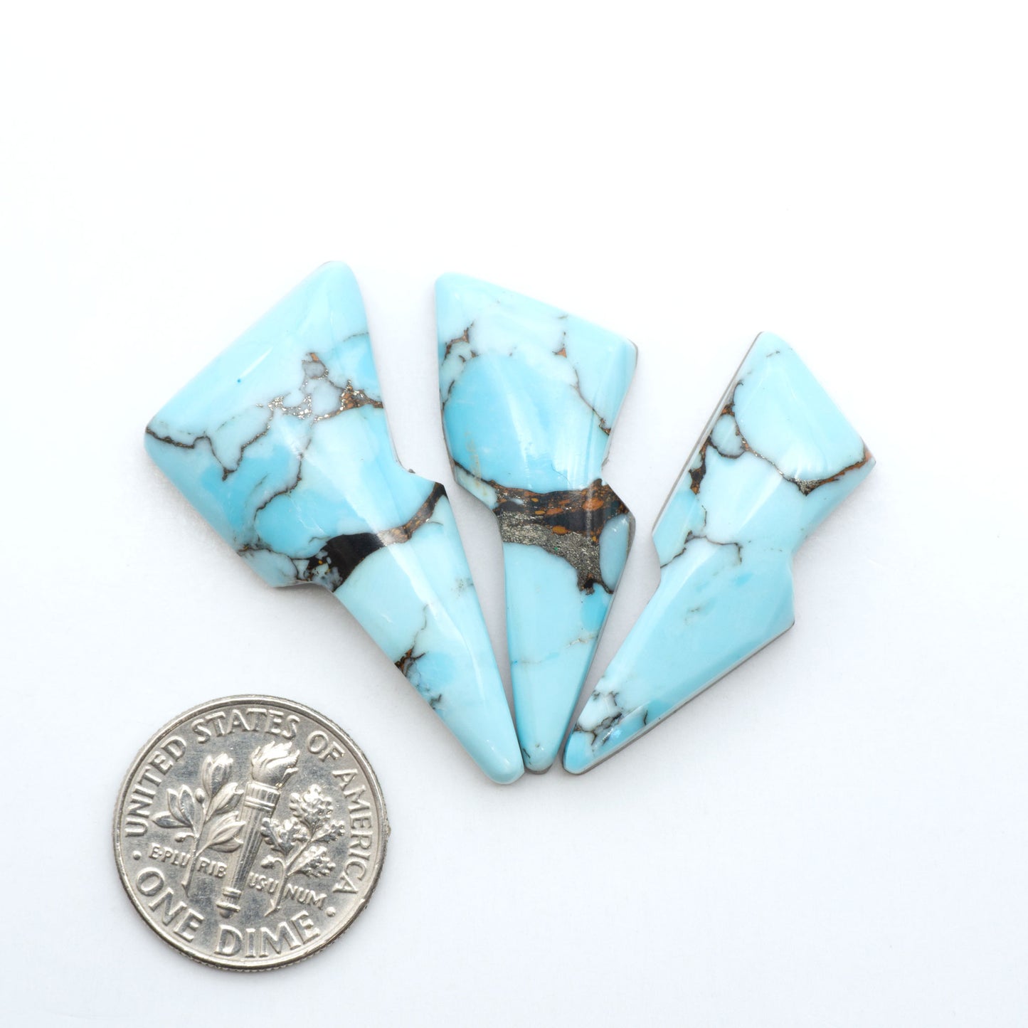 Pressed Turquoise nugget cabochons, composite material with a blue color and dark matrix on a white background, with a US dime for scale.