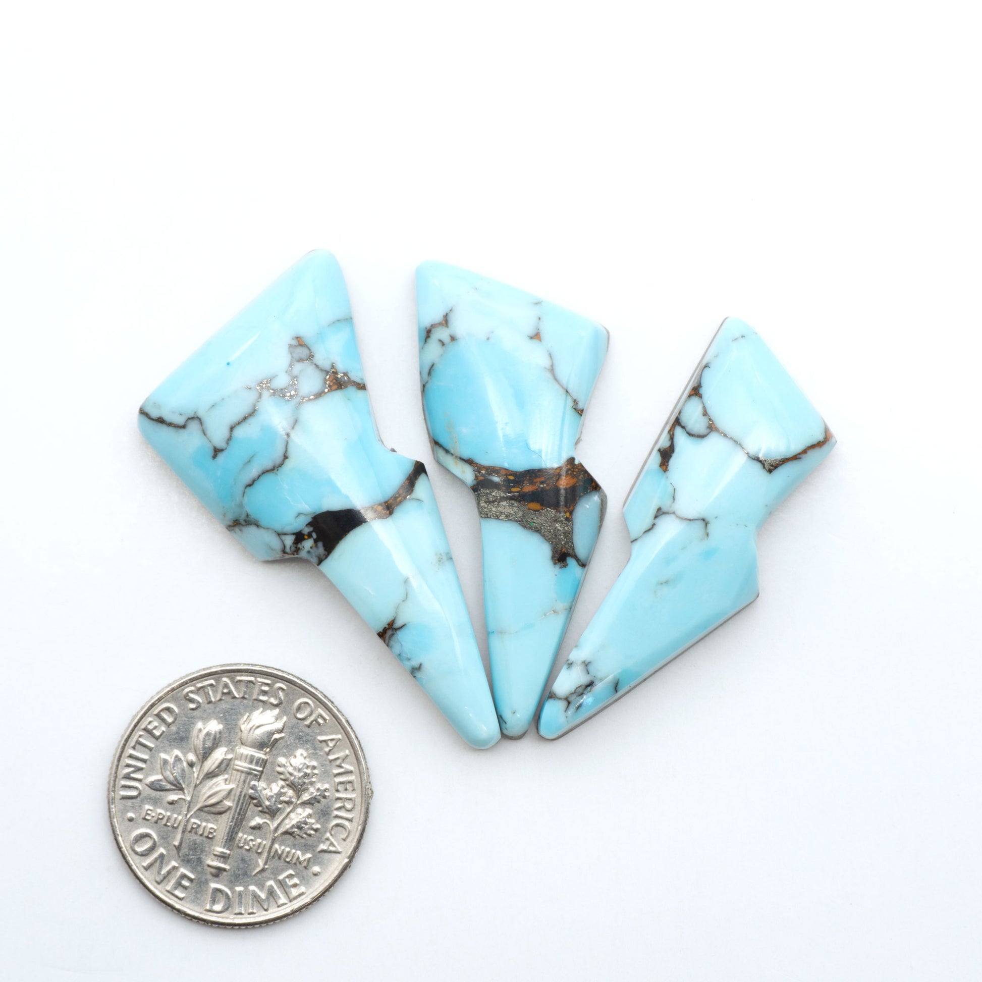 Pressed Turquoise nugget cabochons, composite material with a blue color and dark matrix on a white background, with a US dime for scale.