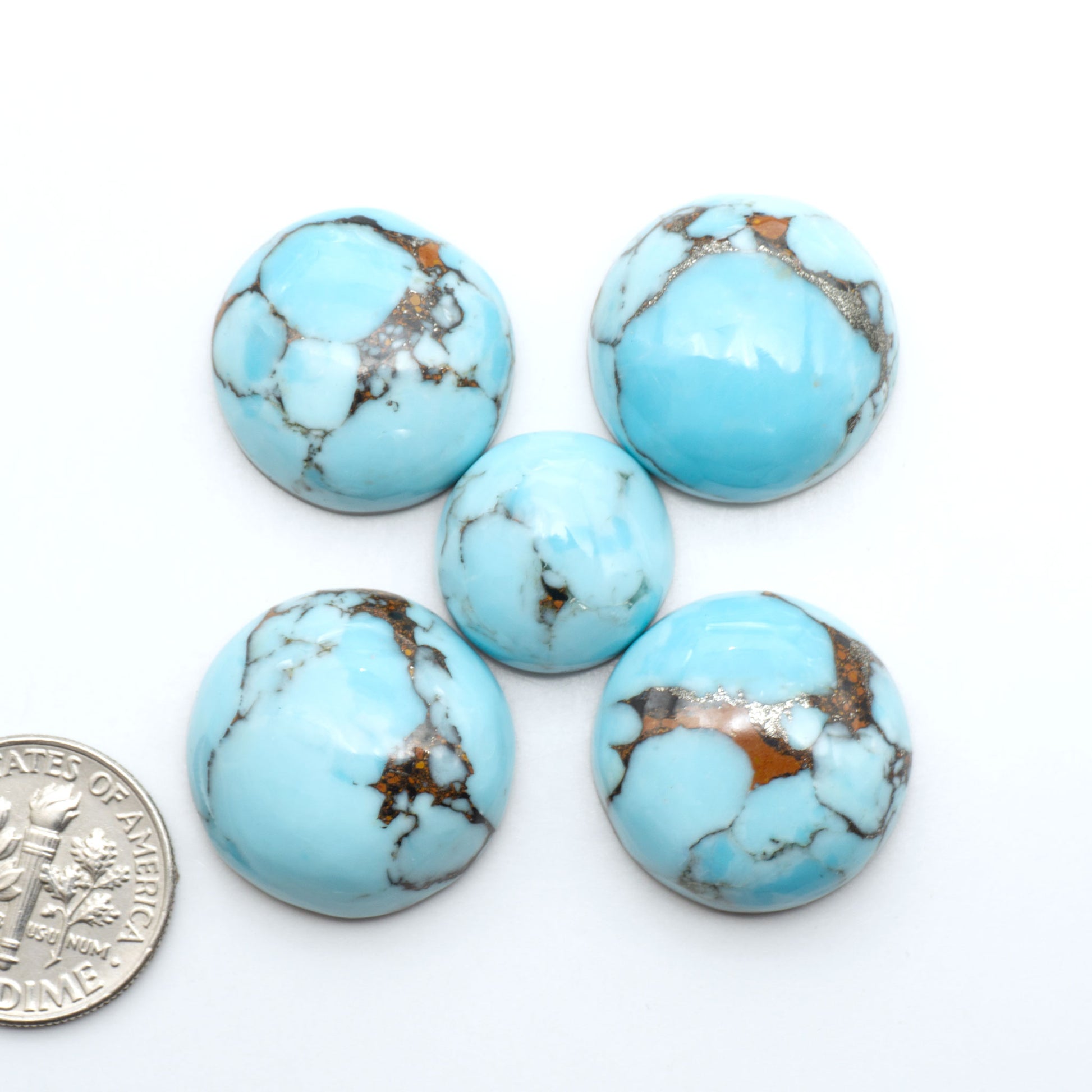 Pressed Turquoise nugget cabochons, composite material with a blue color and dark matrix on a white background, with a US dime for scale.