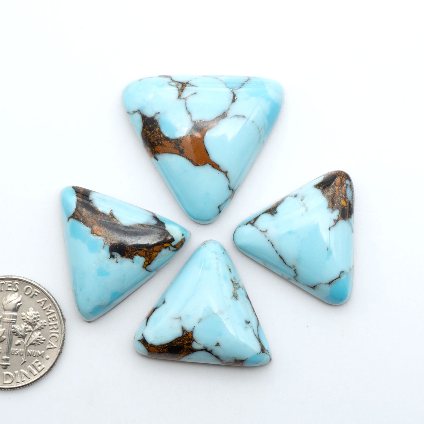 Pressed Turquoise nugget cabochons, composite material with a blue color and dark matrix on a white background, with a US dime for scale.