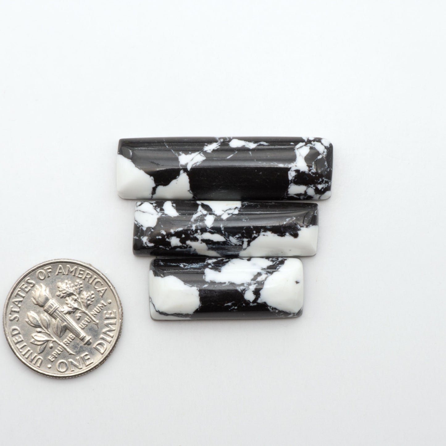 White Buffalo composite cabochons, black and white gemstones on a white background with a US dime for scale