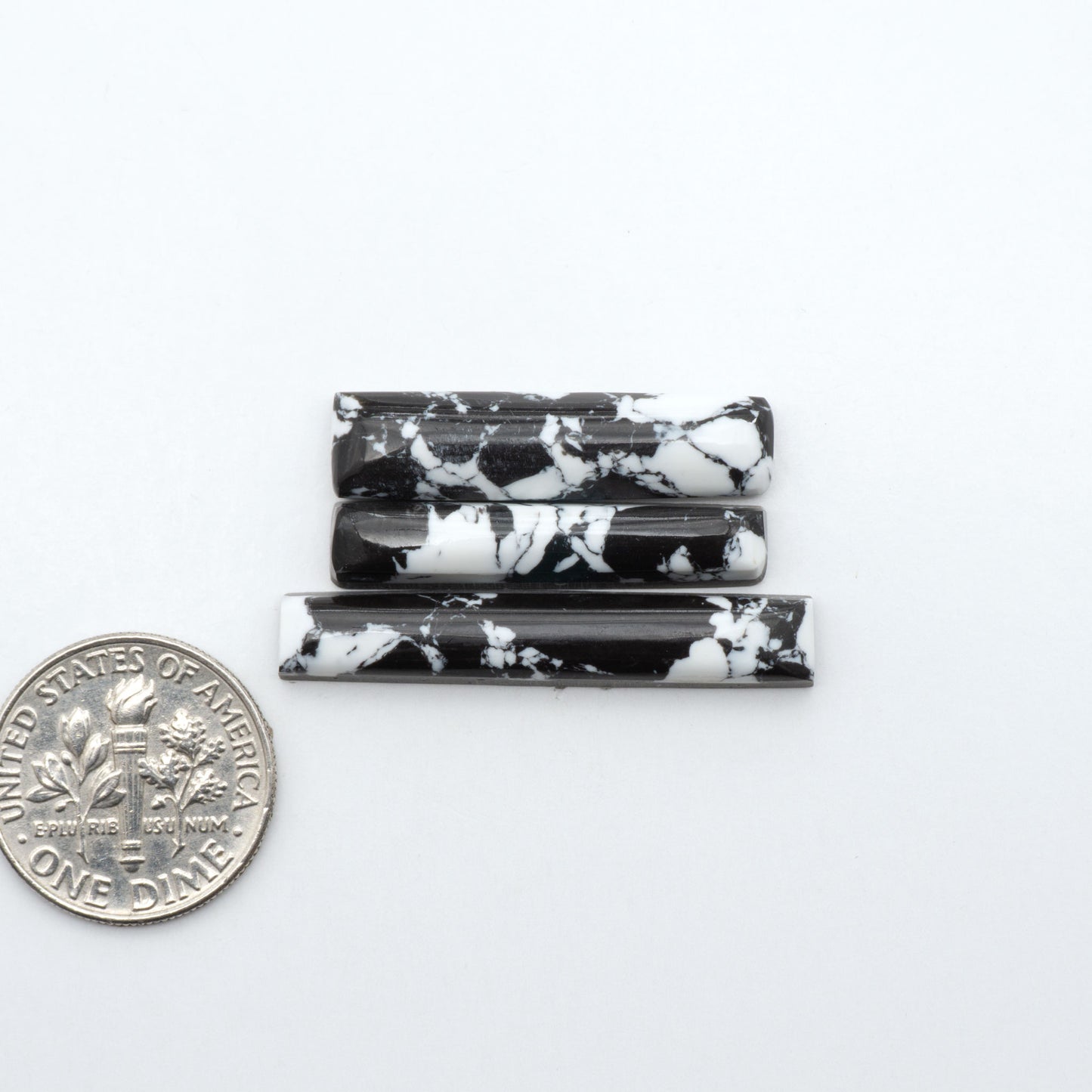 White Buffalo composite cabochons, black and white gemstones on a white background with a US dime for scale