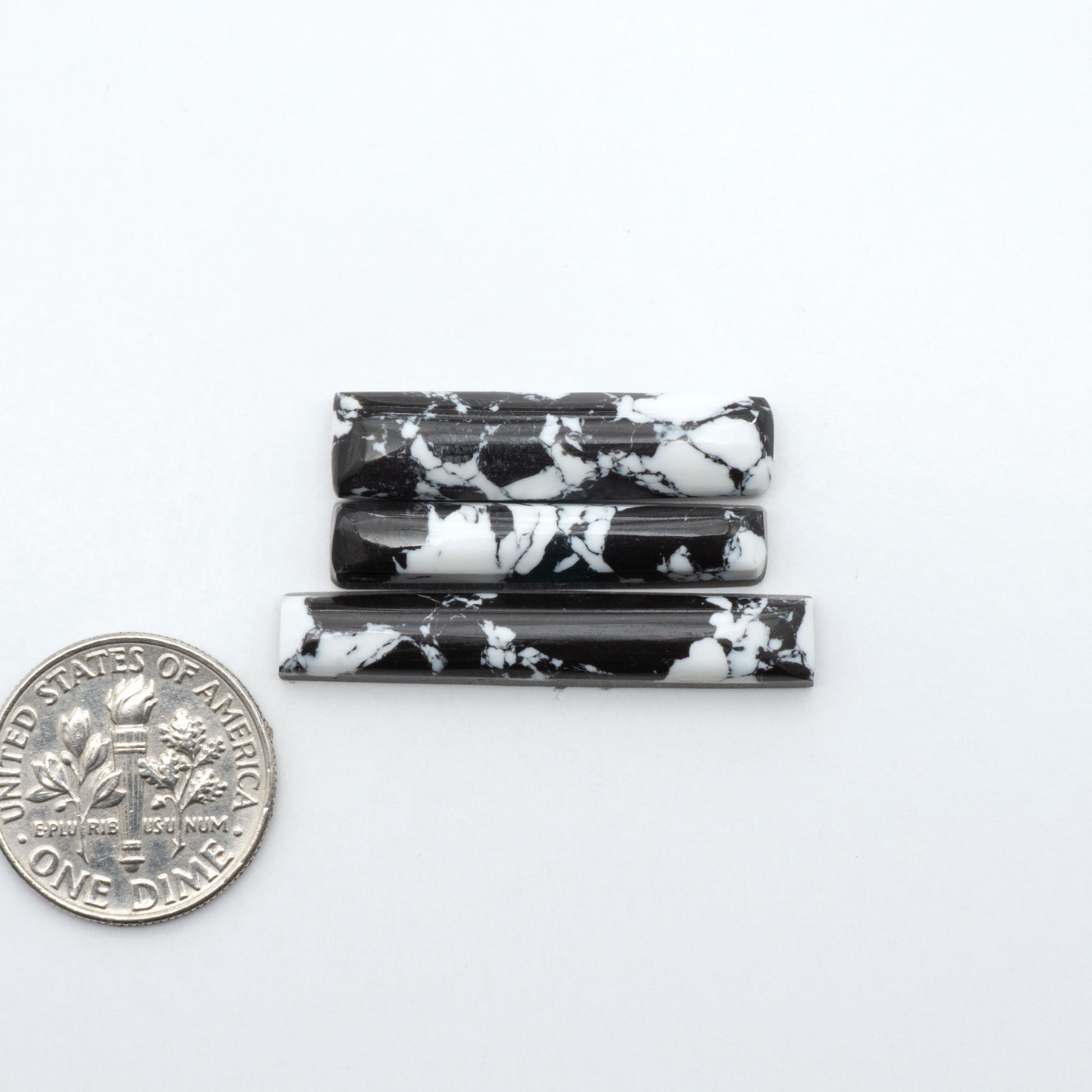 White Buffalo composite cabochons, black and white gemstones on a white background with a US dime for scale