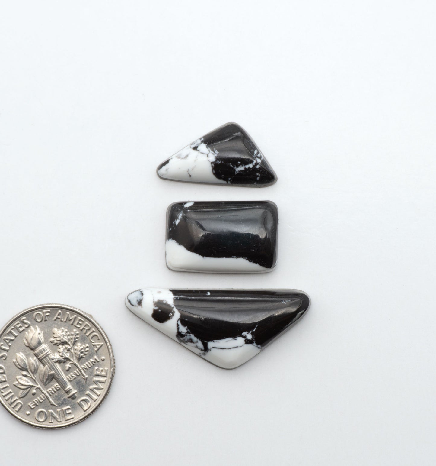 White Buffalo composite cabochons, black and white gemstones on a white background with a US dime for scale