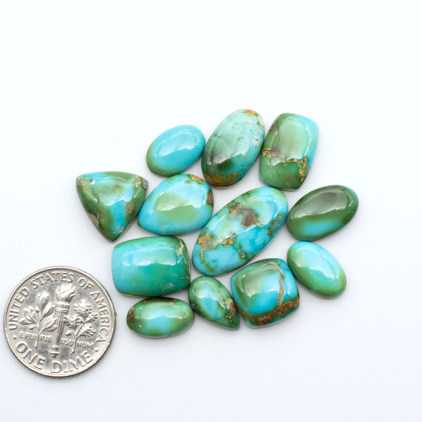 Sonoran Mountain Turquoise cabochons, blue-green color with natural matrix, polished stones on a white background, with a US dime for scale