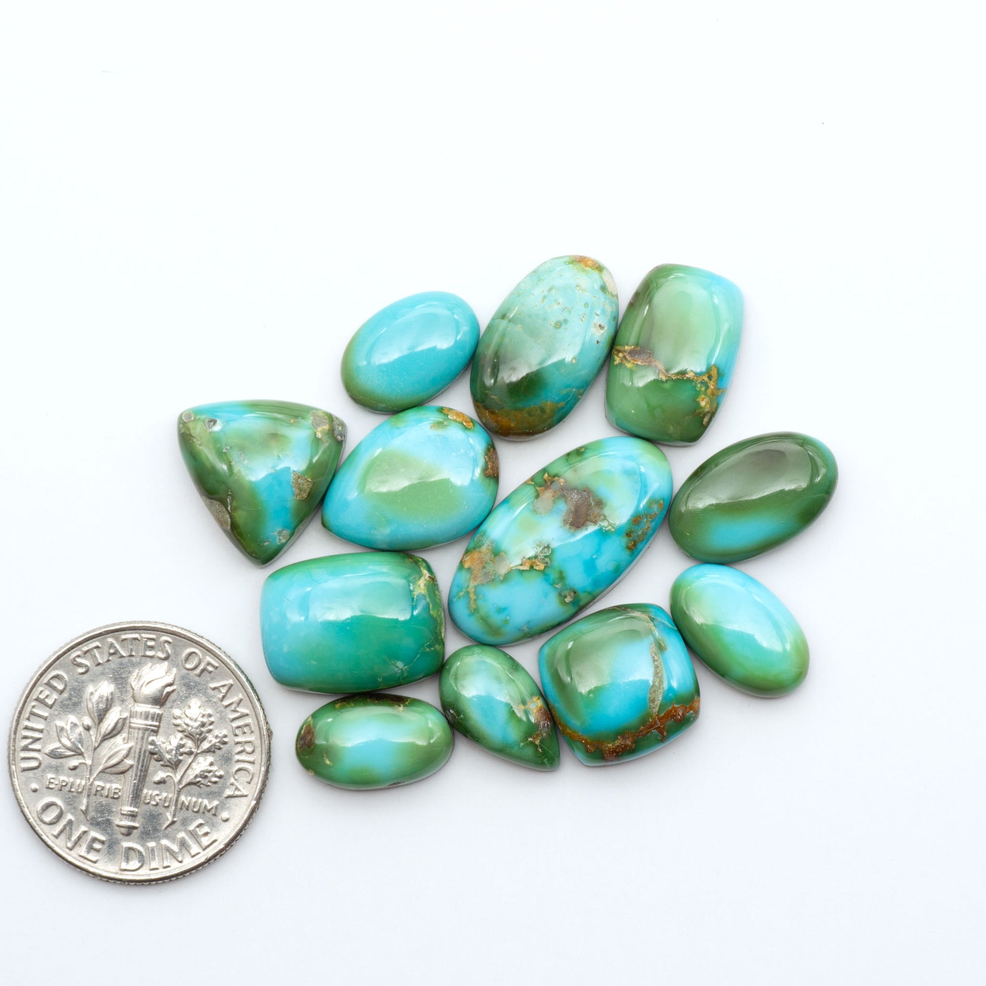 Sonoran Mountain Turquoise cabochons, blue-green color with natural matrix, polished stones on a white background, with a US dime for scale