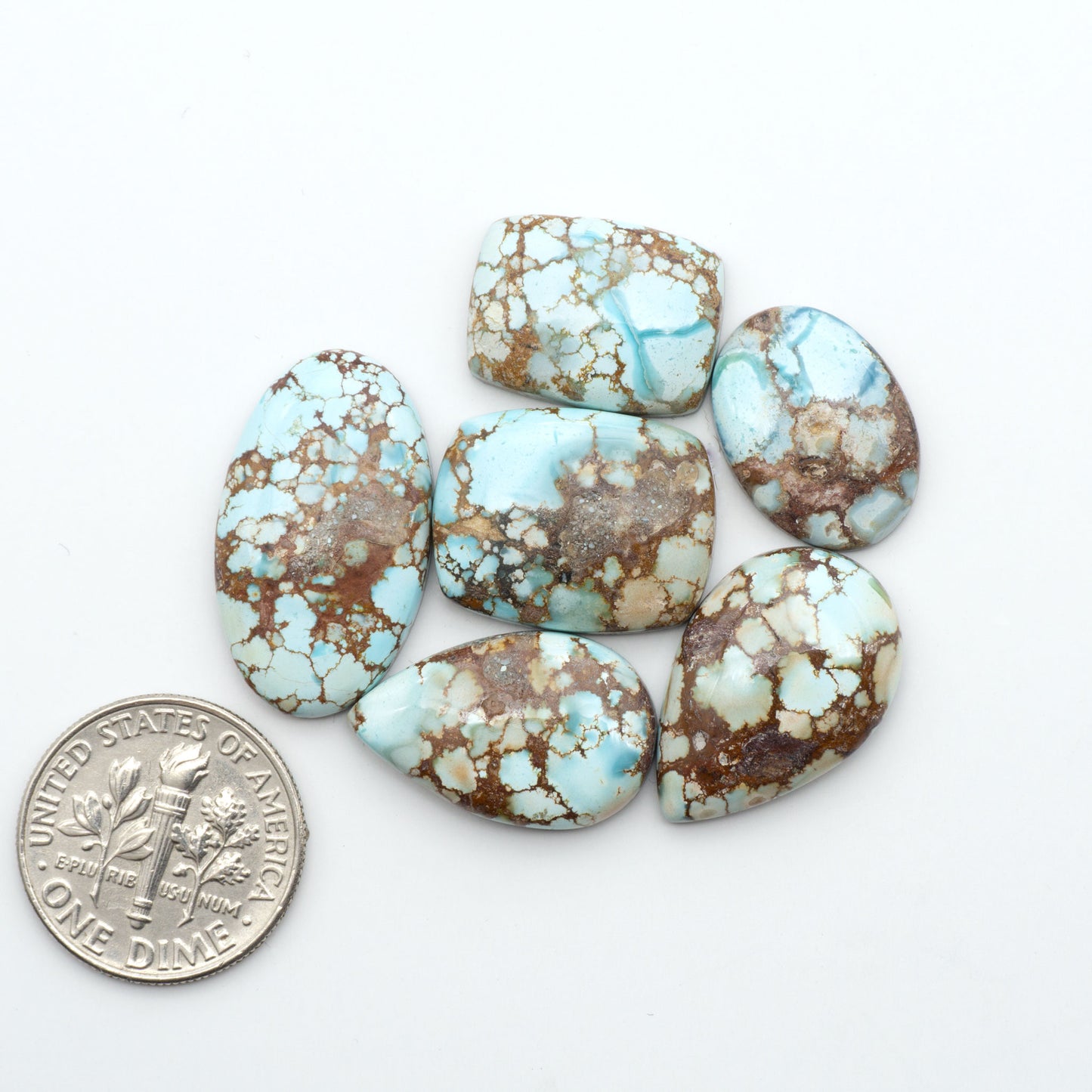 Golden Hills Turquoise cabochons, icy blue to lavender tones with chocolate matrix, polished stones on a white background with a US dime for scale