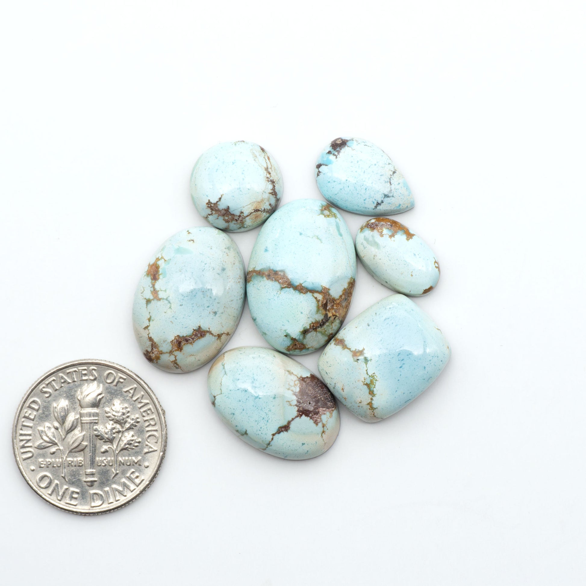 Golden Hills Turquoise cabochons, icy blue to lavender tones with chocolate matrix, polished stones on a white background with a US dime for scale