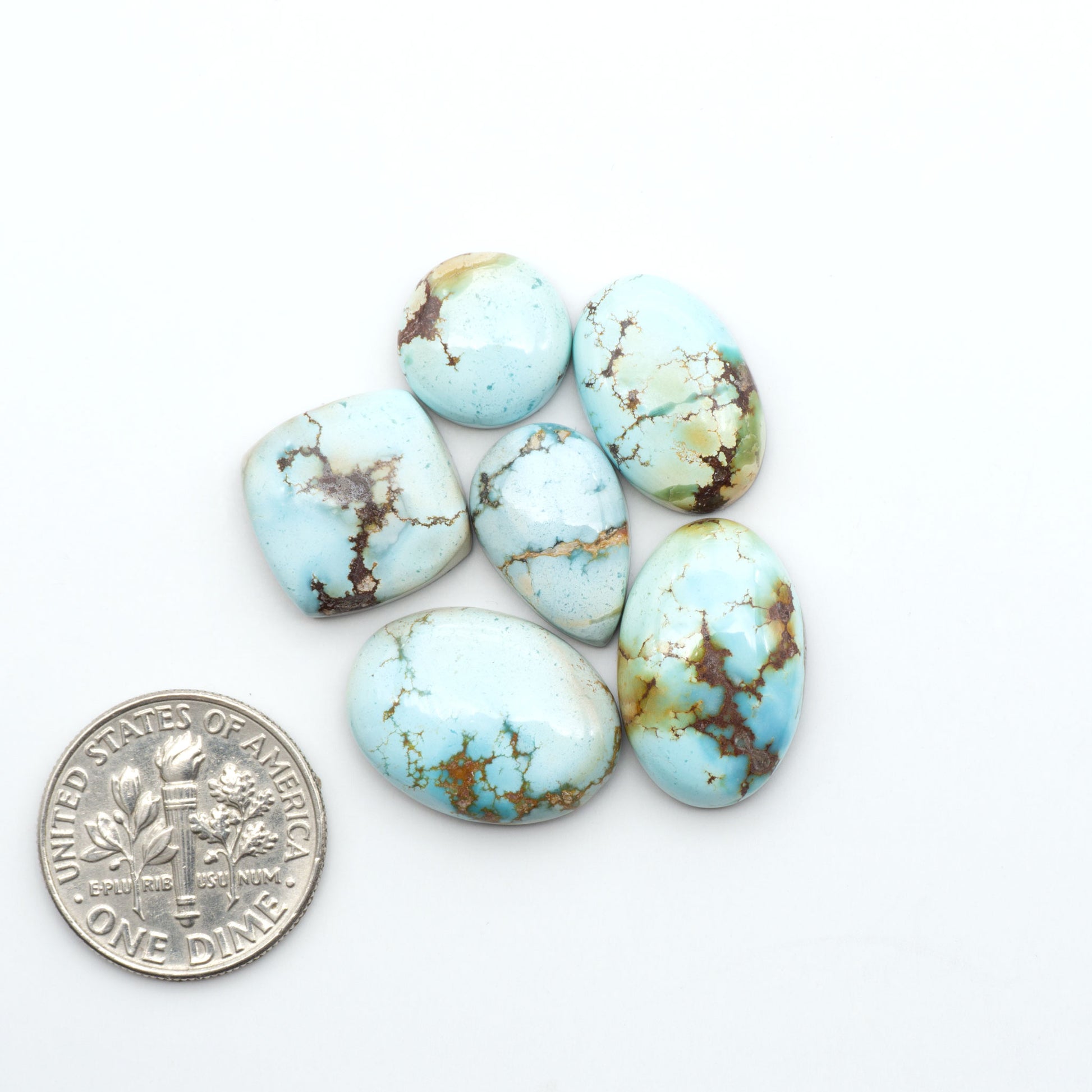Golden Hills Turquoise cabochons, icy blue to lavender tones with chocolate matrix, polished stones on a white background with a US dime for scale