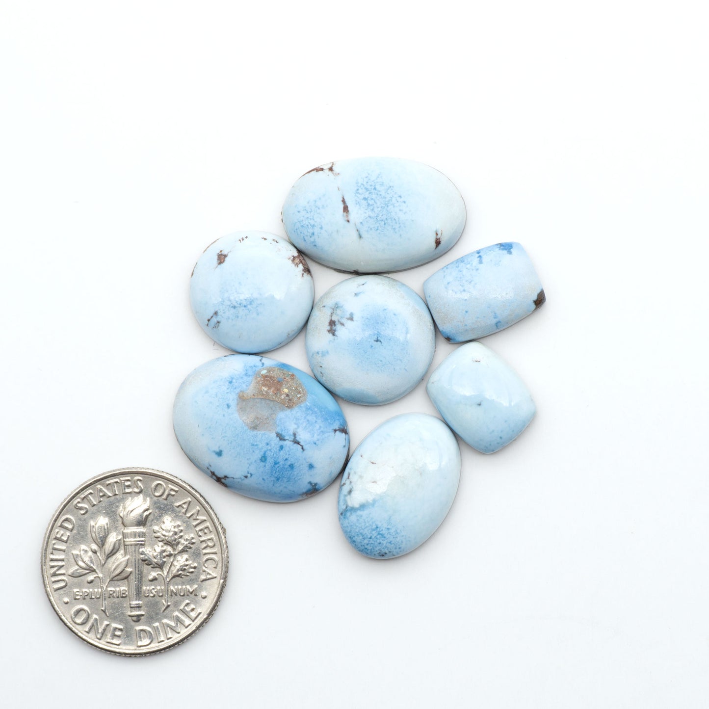 Golden Hills Turquoise cabochons, icy blue to lavender tones with chocolate matrix, polished stones on a white background with a US dime for scale