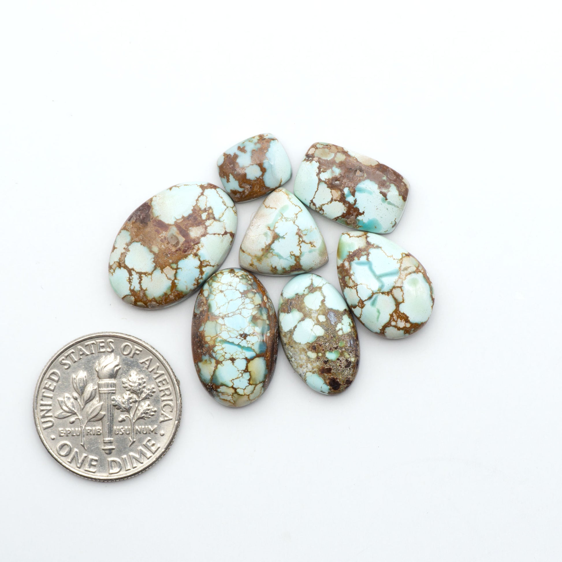 Golden Hills Turquoise cabochons, icy blue to lavender tones with chocolate matrix, polished stones on a white background with a US dime for scale
